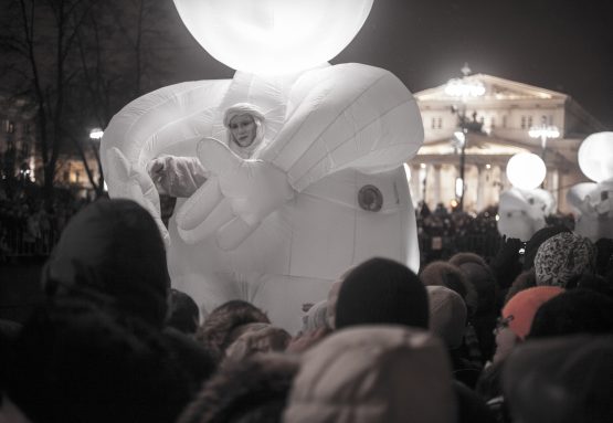 A large balloon-type figure in white parades the streets surrounded by crowds