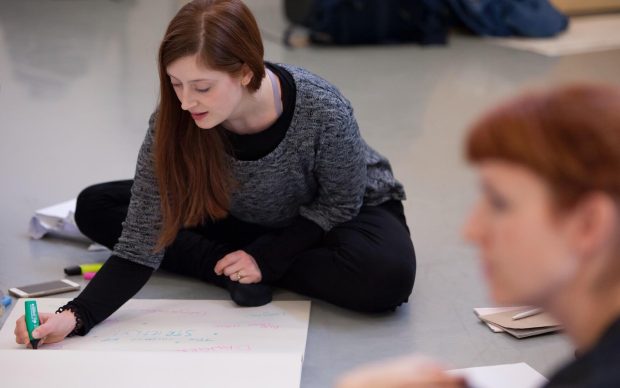 Two dance artists writing on large sheets of paper on the floor