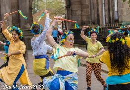 Movema's world dance artists dancing in the street with batons and blue and yellow garlands in hair.