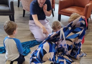 A lady with a group of young children taking part in creative activities with scarves