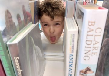 A child peeking through a bookshelf in a library