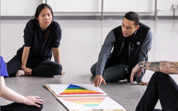 A group of global majority artists sat on the floor in front of a book in discussion