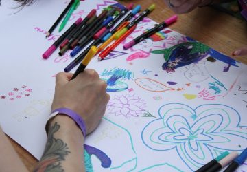 A young persons arm using felt tips to doodle on a large white canvas