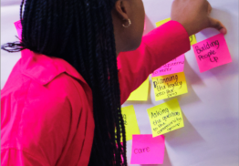 A young Global Majority Artist in a pink top pinning post it notes to a board