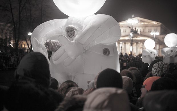 A giant balloon man in a striking white inflatable costume wades through the crowds at a street festival